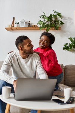 Happy couple enjoys quality time together in their cozy living room, sharing laughter and warmth over laptop clipart