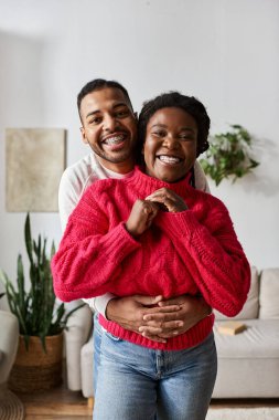 A couple in cozy sweaters embraces warmly on a winter day at home. clipart