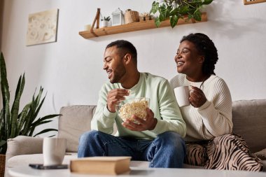Çift kanepede dinlenir, serin bir kış akşamında patlamış mısır ve sıcaklığı paylaşır..
