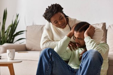 African American couple wearing cozy sweaters during winter, woman comforting her crying partner clipart