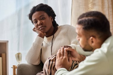 African American man holding hand of his sad girlfriend in their cozy living room clipart