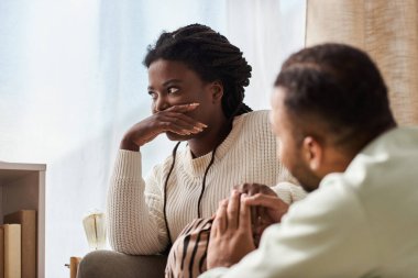 African American man holding hand of his upset girlfriend in their cozy living room clipart