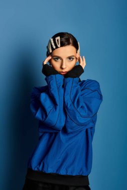 Şık bir kadın şık bir şekilde poz veriyor, saç tokalarını mavi bir fonda sergiliyor..