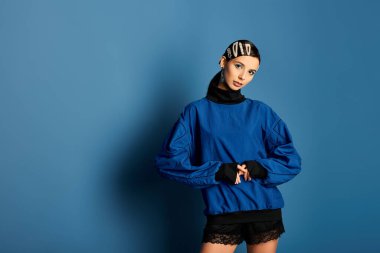 Şık bir genç kadın şık kıyafetini cesur mavi bir arka planda sergiliyor, kendinden emin..