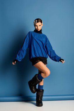 Modaya uygun genç bir kadın mavi bir stüdyoda kendine güvenerek poz veriyor..