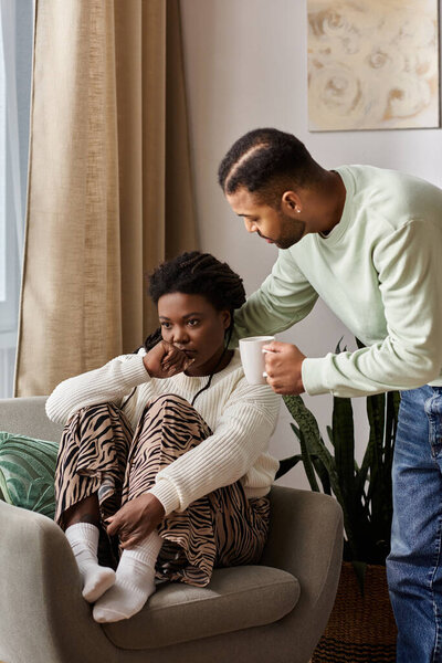 African American man with cup comforting his worried partner in their cozy living room