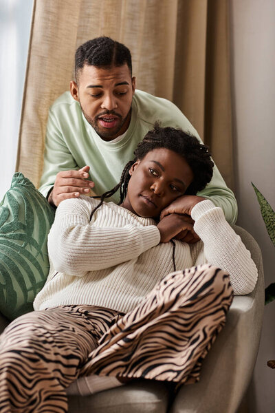 African American man comforting his sad girlfriend in their cozy living room