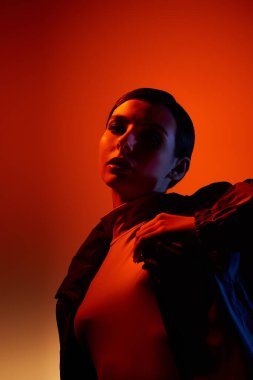 Genç bir kadın şık kıyafetlerini ve makyajını canlı bir stüdyoda zarifçe poz verirken sergiliyor..