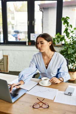 Parlak ve cezbedici çalışma alanı çalışırken kahvesini yudumlayan odaklanmış genç bir kadın içeriyor.