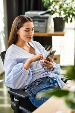 Beautiful brunette woman interacts with her smartphone in a bright office space, smiling. clipart