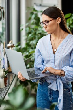 Brunette woman types intently on her laptop while surrounded by vibrant plants. clipart