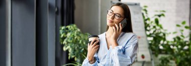Genç bayan bir kahve fincanı tutuyor ve telefonda konuşurken hafifçe gülümsüyor..