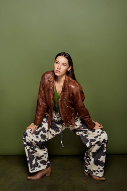 Esmer kadın deri ceket ve desenli pantolonuyla tarzını sergiliyor, kendine güvenerek poz veriyor..