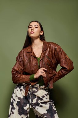 Esmer kadın, bir stüdyoda deri ceket ve eşsiz pantolonuyla tarzını sergiliyor..