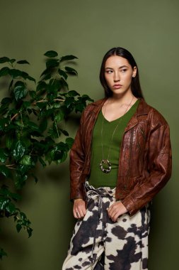 Esmer güzellik, kahverengi ceketli ve sakin bir ortamda desenli pantolonlu bir şekilde sergileniyor..