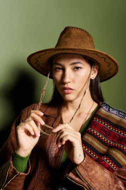Güzel esmer kadın eşsiz moda anlayışını sergilerken güneş gözlüğünü tutuyor..