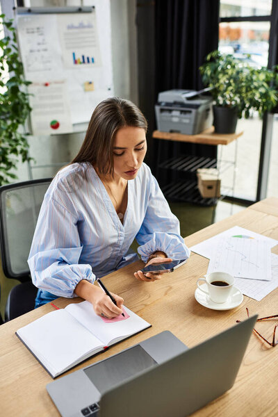Brunette woman writing notes while using her smartphone in a stylish office environment