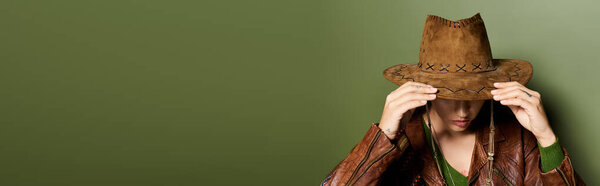 Beautiful young woman adjusts her western hat while showcasing a chic outfit in soft light