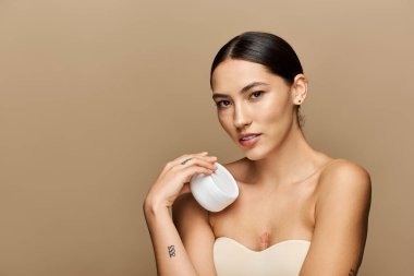 Esmer kadın elinde bir cilt ürünüyle güzellik ve güven sergiliyor..