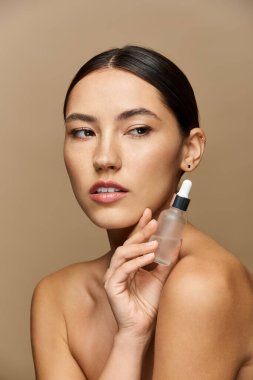 Genç bir esmer kadın elinde bir serum şişesi tutuyor, parlak cildini parlaklaştırıyor..