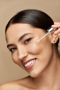 Genç esmer kadın, genç tenine besleyici serum sürerken gülümsüyor..