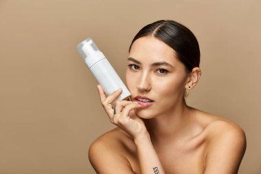 Young woman showcases her radiant skin while holding a skincare product in a calm atmosphere. clipart