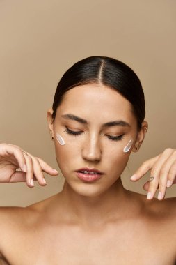 Young beautiful brunette woman applies skincare product while relaxing in a minimalistic space. clipart