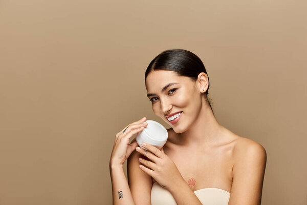 Молодая брюнетка демонстрирует свою сияющую кожу, держа контейнер для кожи.