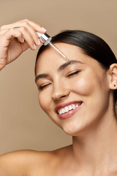 Молодая женщина ярко улыбается, нанося сыворотку на лоб в спокойной атмосфере.