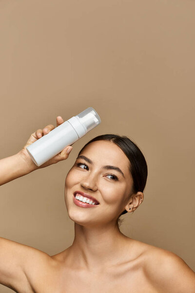 Beautiful brunette woman applies a skincare product while smiling against a soft, warm backdrop