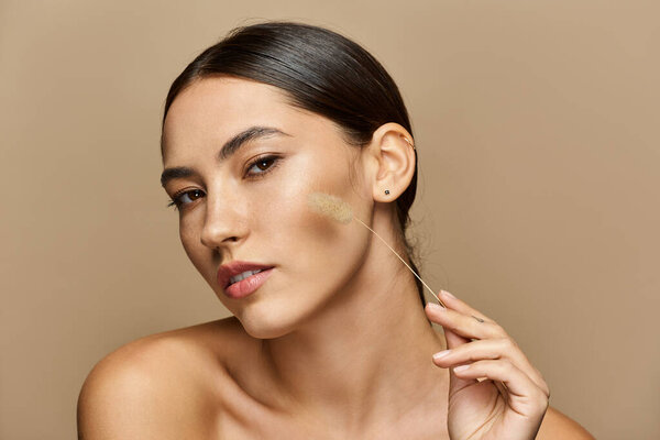 Молодая женщина подчеркивает свою природную красоту элегантной позой на мягком фоне.