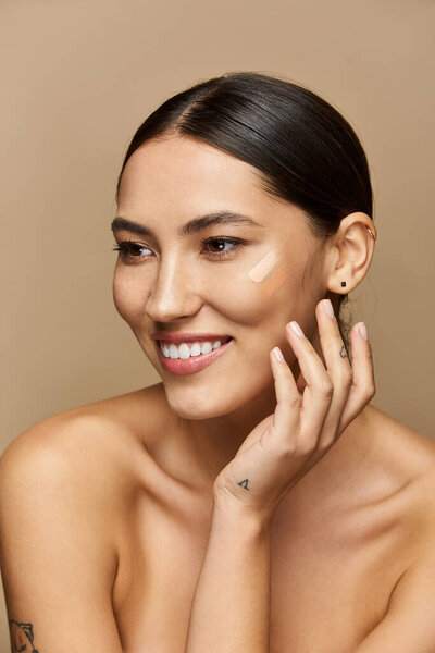 Брюнетка тепло улыбается, нанося макияж на нейтральный фон..