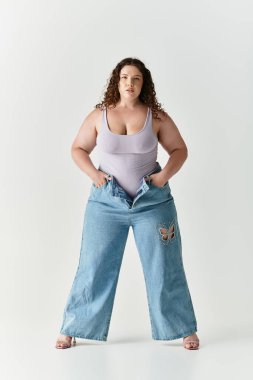 Genç bir kadın moda anlayışını minimalist bir stüdyo arka planında moda kıyafetleriyle kucaklıyor..
