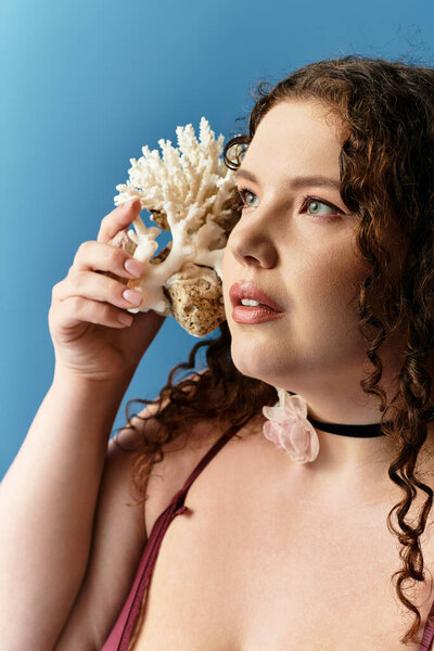Young woman with curly hair in a trendy outfit poses elegantly with a coral decoration.