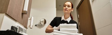 Meşgul genç bir kadın modern bir otel banyosunda yeni havlular hazırlıyor..