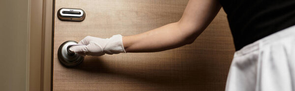 A young woman dressed beautifully opens a hotel door with grace and hospitality at dusk.