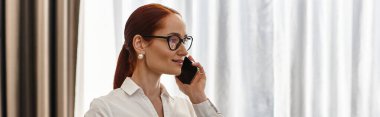 Young woman with glasses talks on the phone, showcasing confidence in a modern environment. clipart