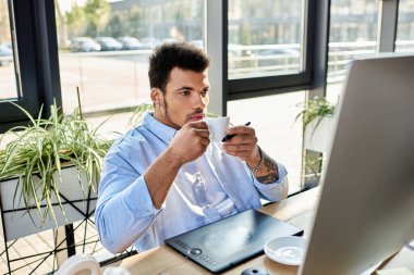 Odaklanmış adam kahvesini yudumluyor ve şık, güneşli bir ofis ortamında dijital tasarım üzerinde çalışıyor..