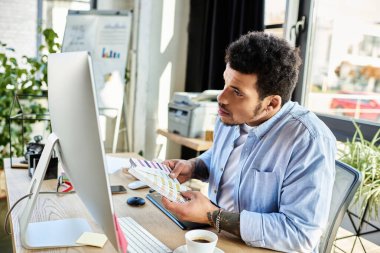 A handsome man reviews color swatches at a sleek desk in a cozy office. clipart