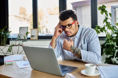 Yakışıklı bir adam, modern bir ofis ortamında dizüstü bilgisayarının başında çalışırken derin düşüncelere dalmış..