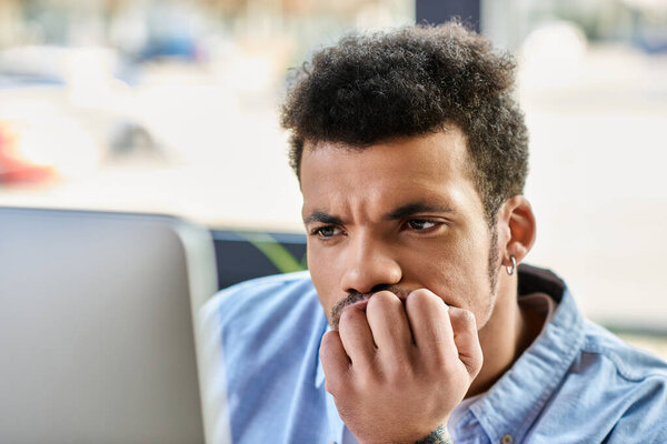 Handsome man ponders thoughtfully, fingers touching his chin, surrounded by a lively cafe setting.