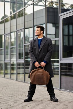 Şık bir palto giymiş bir adam, şık bir yapının yanında bir çanta tutarken kendine güvenir..