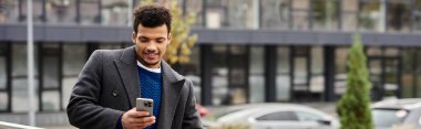 A young man enjoys his smartphone in an urban setting, exuding confidence and style. clipart