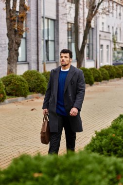 Yakışıklı bir adam güvenli bir şekilde ağaçlarla kaplı bir caddede yürüyor, gevrek şehir havasının tadını çıkarıyor..
