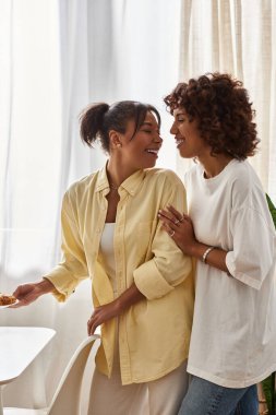 İki genç kadın, şık evlerinde, birbirlerine sarılarak kahvaltıdan keyif alırlar..