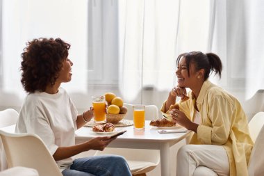 İki Afro-Amerikan kadını, neşeli ve modern bir ortamda aynı kahkahayı ve kahvaltıyı paylaşıyor..