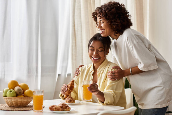 Молодая лесбийская пара разделяет любящий завтрак, наслаждаясь друг другом и смеясь.