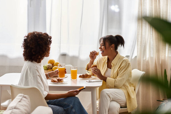 Две молодые чернокожие женщины вместе завтракают в своей солнечной, стильной квартире.