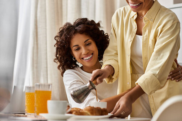 Две молодые женщины наслаждаются уютным завтраком, делясь улыбками и моментами в своей стильной квартире.
