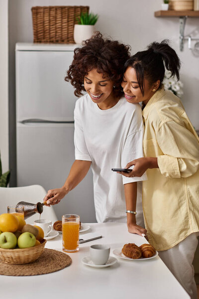 Две молодые женщины делятся смехом и любовью, готовя завтрак на яркой, современной кухне.